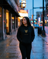 Woman wearing the Lioness Fire Crop Hoodie in Black on a city street at dusk
